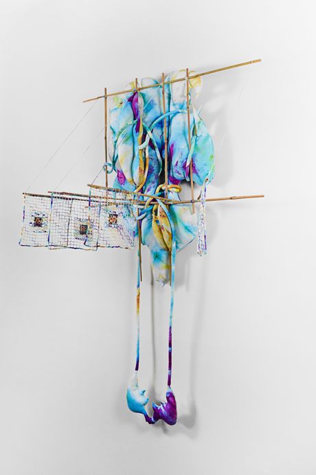 A wall soft sculpture tie dyed in hues of violet, blue, and yellow with filet lace and netting elements framed in bamboo that are tied using square lashing knots. Within the filet lace is an embedded gay pornographic image using a sublimation dye technique.