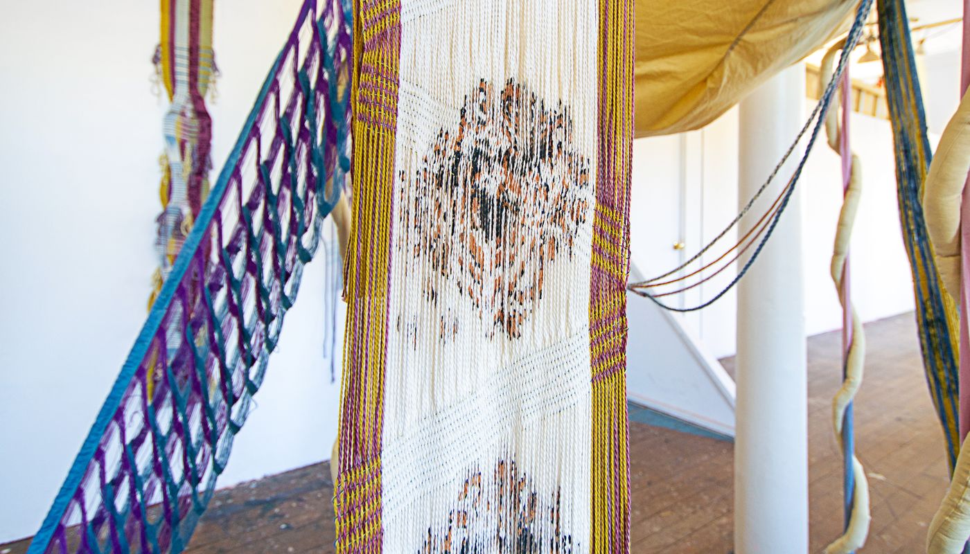 Colorful woven forms using backstrap weaving on fabric posts dyed with goldenrod, sappanwood, mulberry leaves, gardenia, annatto, logwood, and indigo.