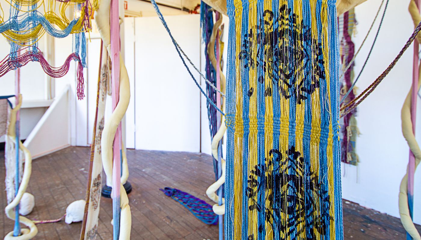 Colorful woven forms using backstrap weaving on fabric posts dyed with goldenrod, sappanwood, mulberry leaves, gardenia, annatto, logwood, and indigo.