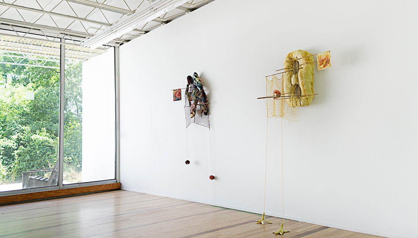 Installation shot taken in the Roger Brown Residency studio of two wall soft sculptures with filet lace and netting elements framed in bamboo that are tied using square lashing knots.